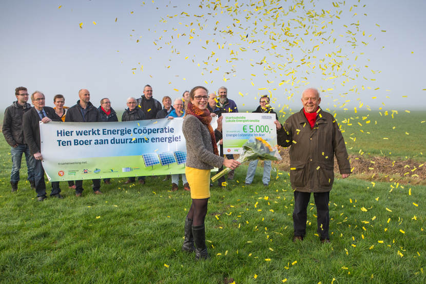 Foto waarop gedeputeerde Nienke Homan op feestelijke wijze een cheque met subsidie overhandigt aan de initiatiefnemers van de zonneweide Ten Boer