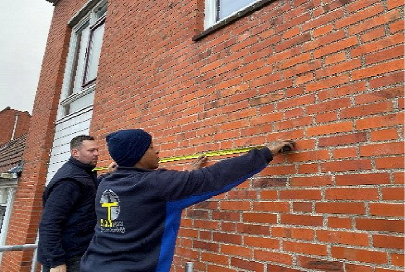 Twee mannen doen meetwerk bij een bakstenen muur